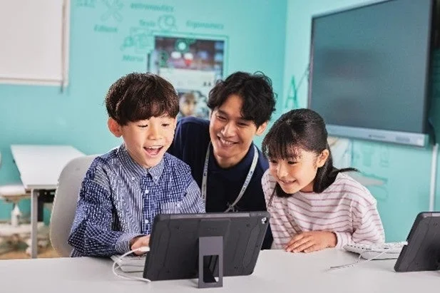 明るい教室で、男性の先生がタブレットを使って2人の子供たちに教えている