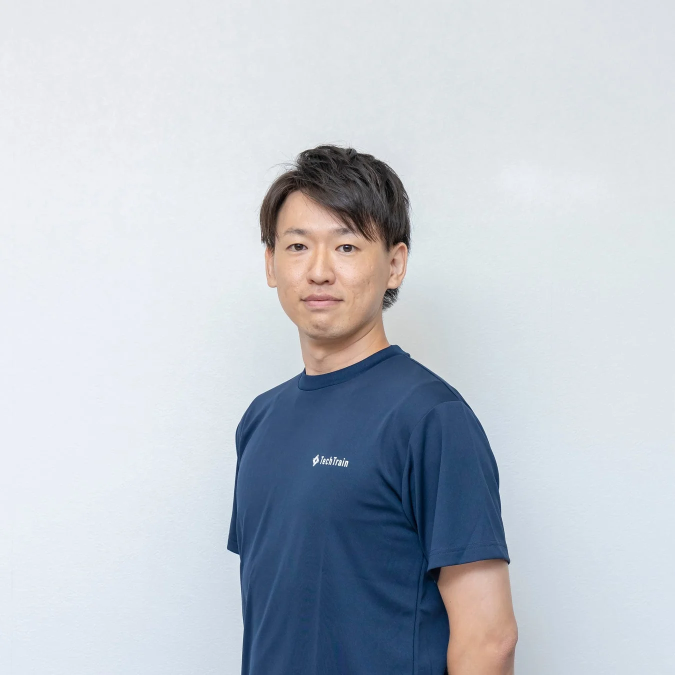 TechTrainのロゴ入り紺色のTシャツを着た男性