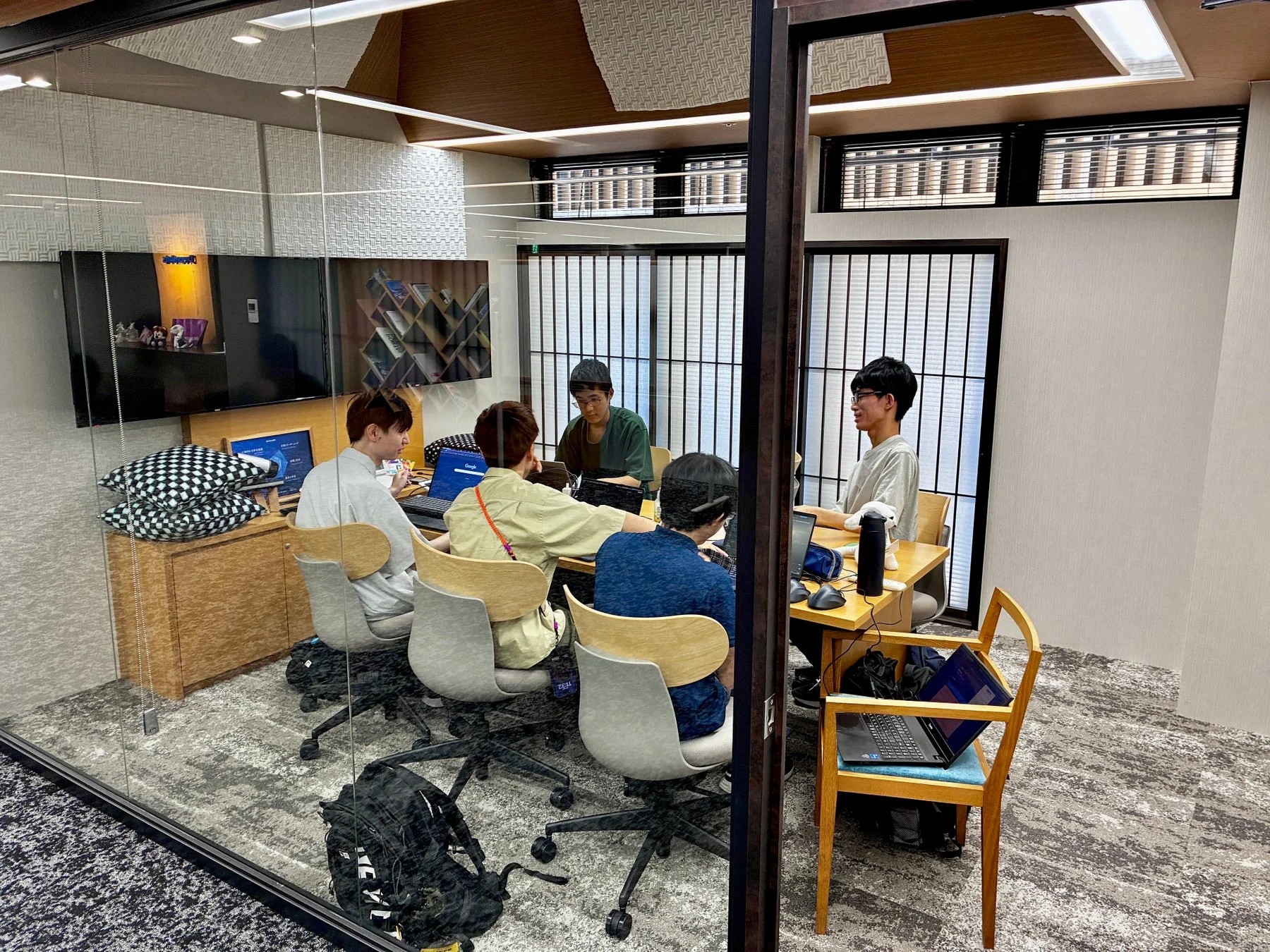 モダンな会議室で5人の若者がノートパソコンに向かい、共同で作業や勉強をしている様子